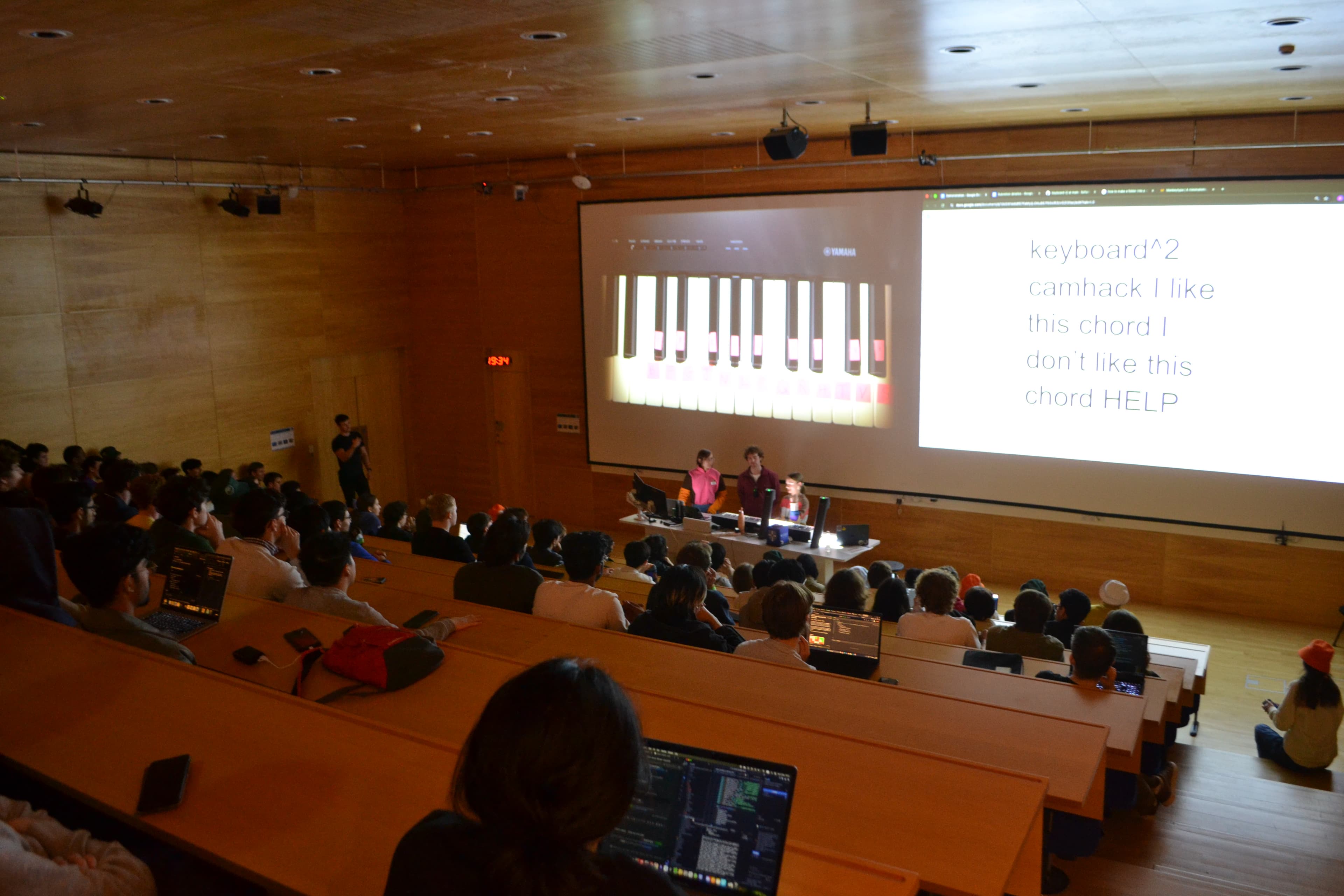 A lecture theatre audience watching the Keyboard² demo, with a piano interface and typed text on the projector screen