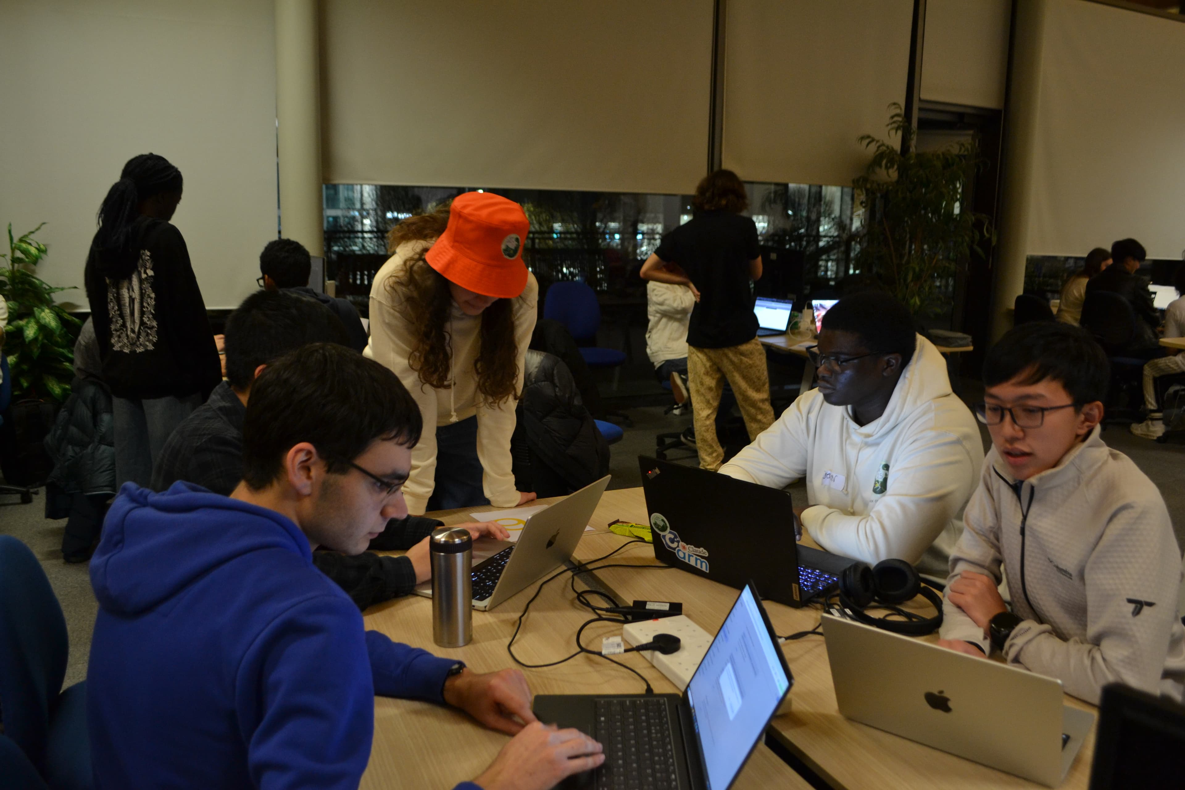 An organiser in an orange bucket hat leaning over to check on a team working at their laptops